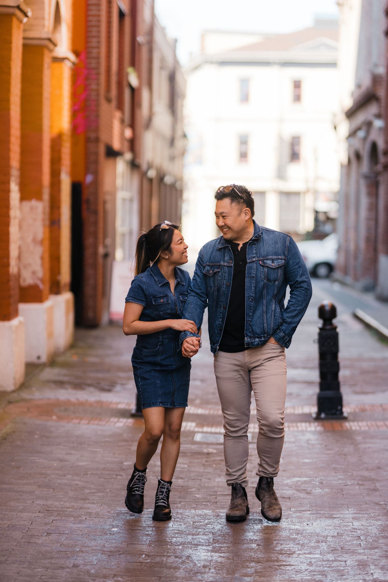 Happy couple in denim walking hand-in-hand through a charming wet cobblestone alley.
