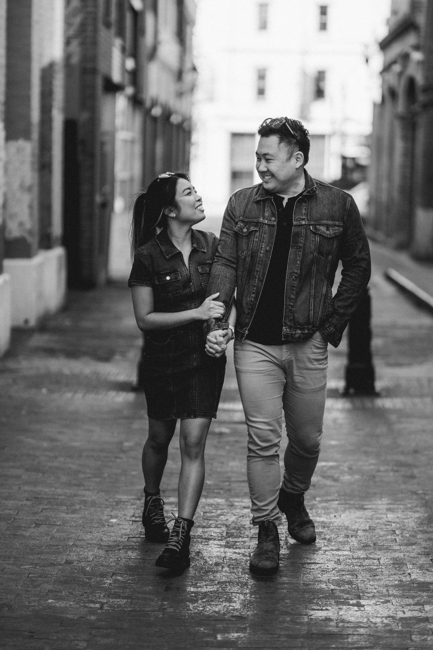 Happy Asian couple walk hand-in-hand laughing together down a wet cobblestone alley.