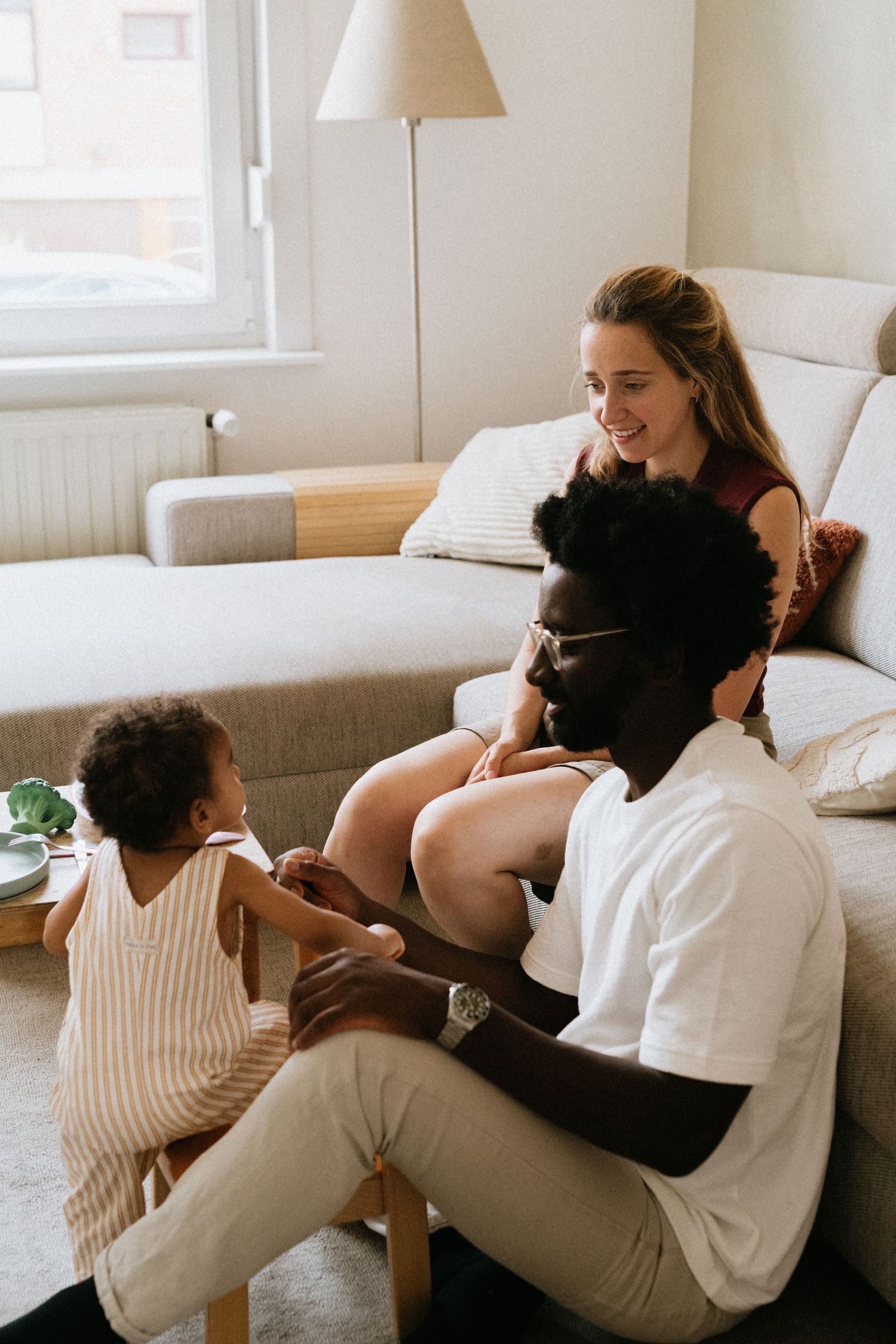 A happy interracial family relaxing together in a cozy living room, with parents smiling at their young toddler.