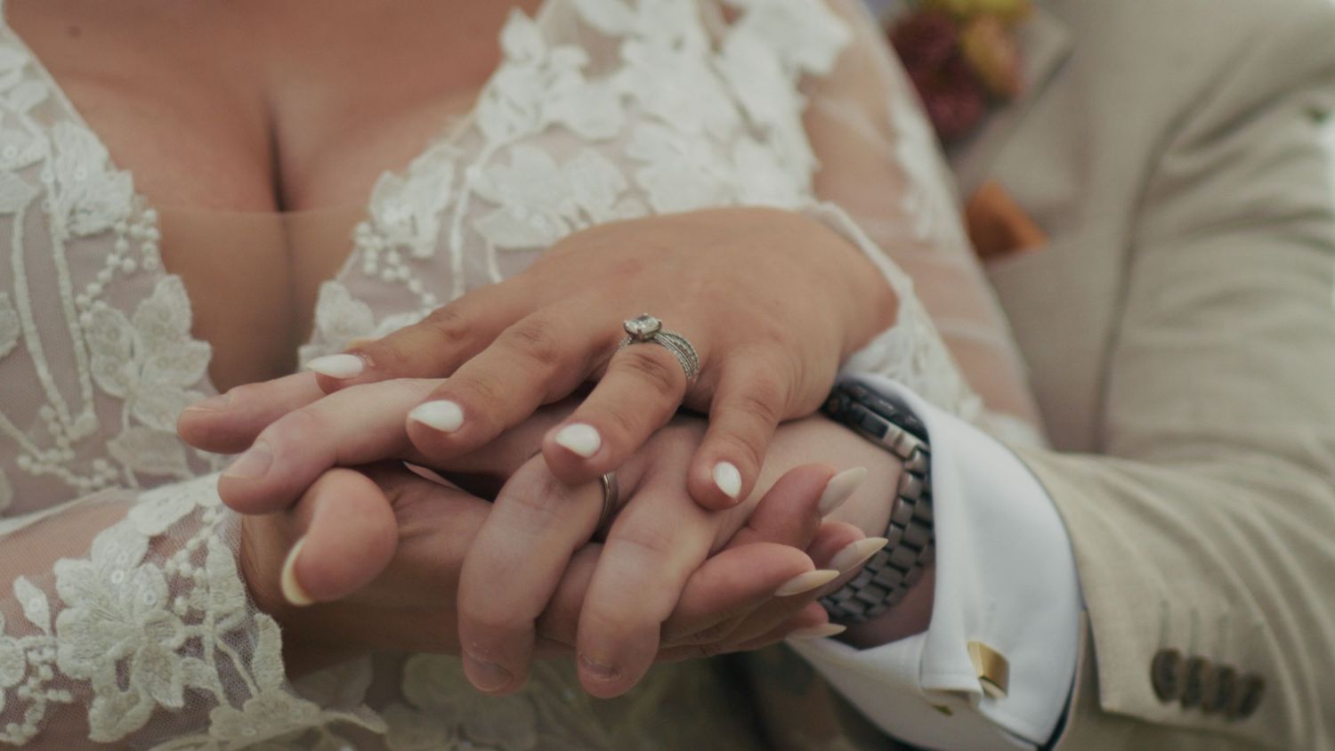 Close-up of bride and groom holding hands, showcasing wedding rings and lace bridal gown.