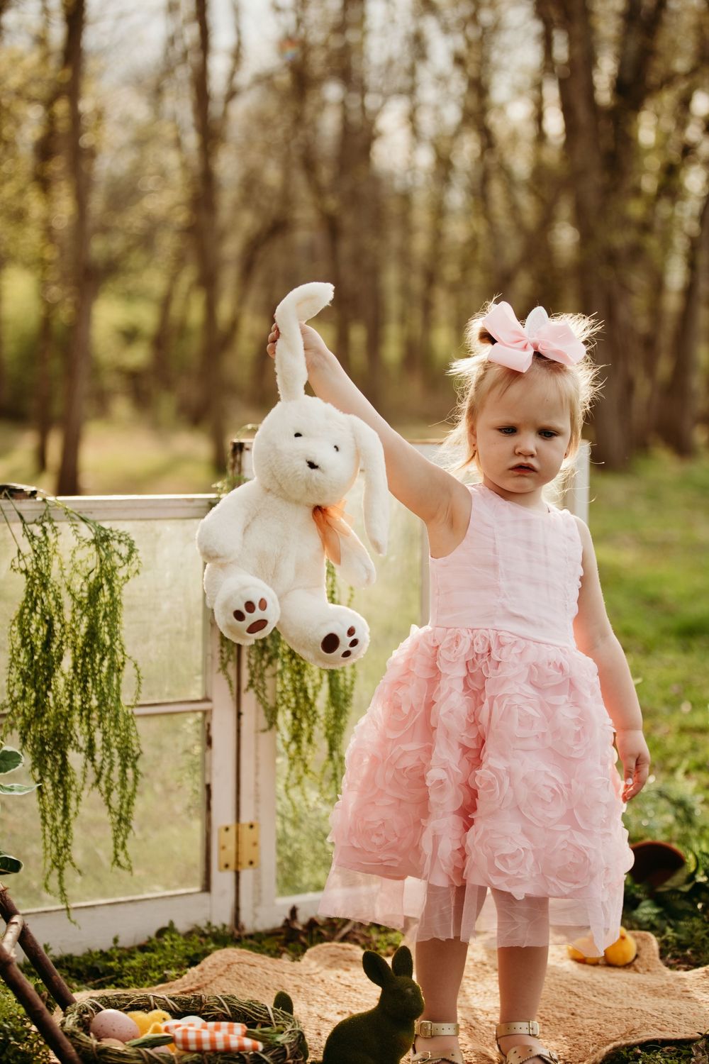 Toddler girl in pink dress holding white bunny stuffed animal outdoors.