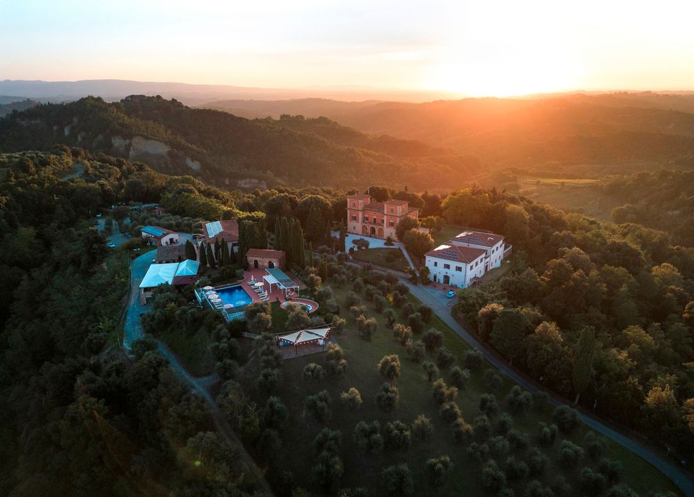 Aerial sunset view of Tuscan villa estate surrounded by lush green hills and olive trees.