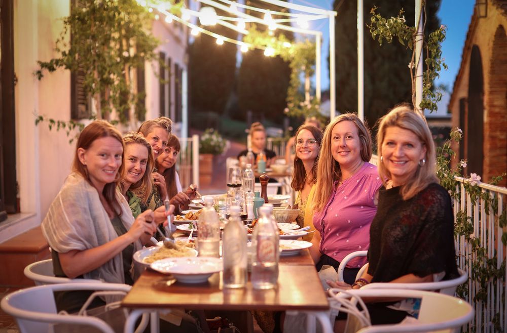 Group of women enjoying dinner together at outdoor restaurant table in warm evening light.