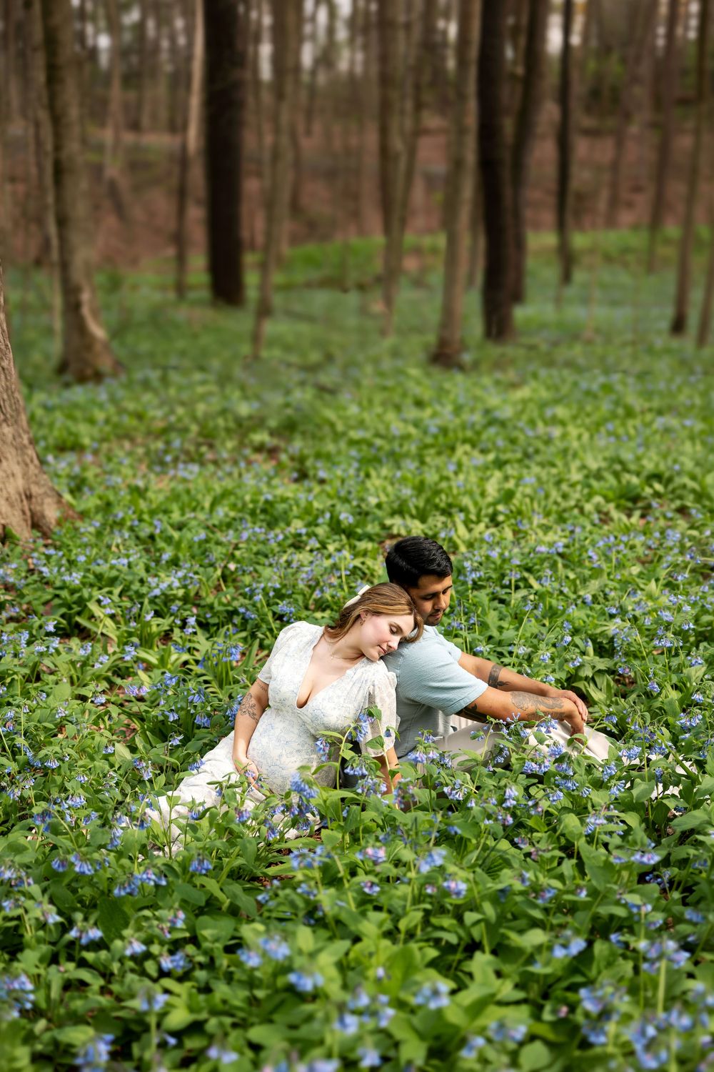 Couple sitting together in a woodland floor covered in blue spring wildflowers.