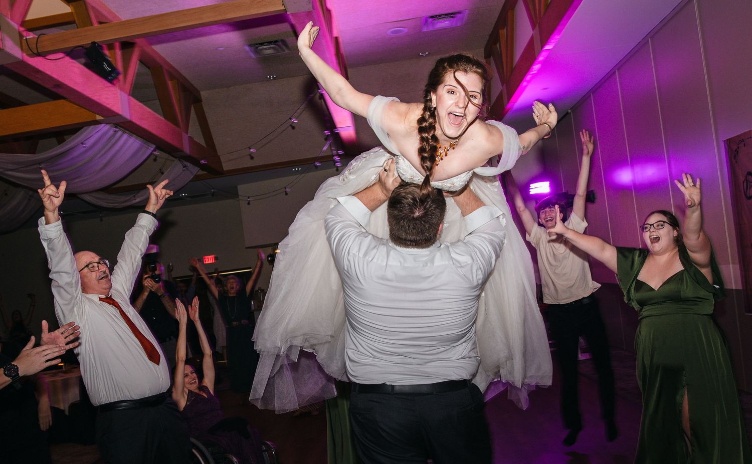 Black and white wedding reception photo of bride dancing joyfully among guests on the dance floor.