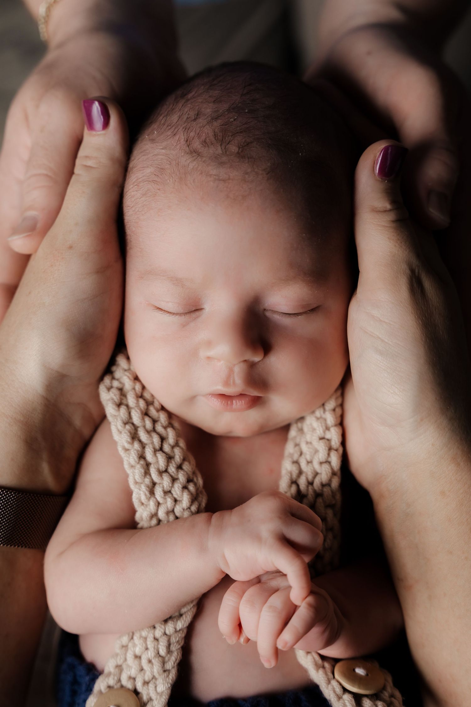 Newborn baby sleeping peacefully in parents hands, wrapped in a knit blanket.