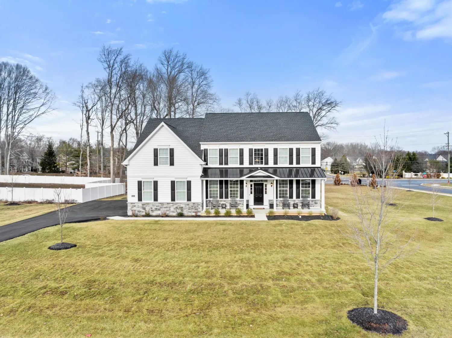 White two-story colonial home with covered porch, black shutters, and manicured lawn surrounded by mature trees.