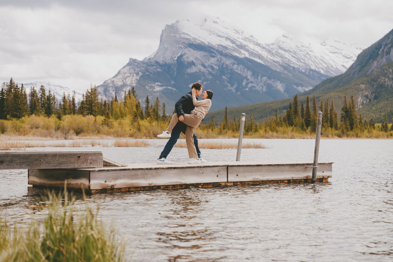 Couple embracing on a dock at Vermilion Lakes with snow-capped Mount Rundle in Banff National Park.