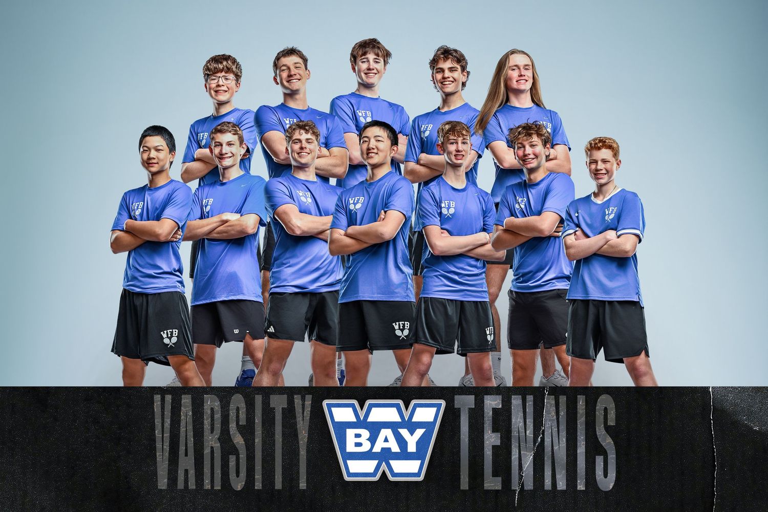 Bay Varsity Tennis team photo with players in blue uniforms posing together against a light gray background.