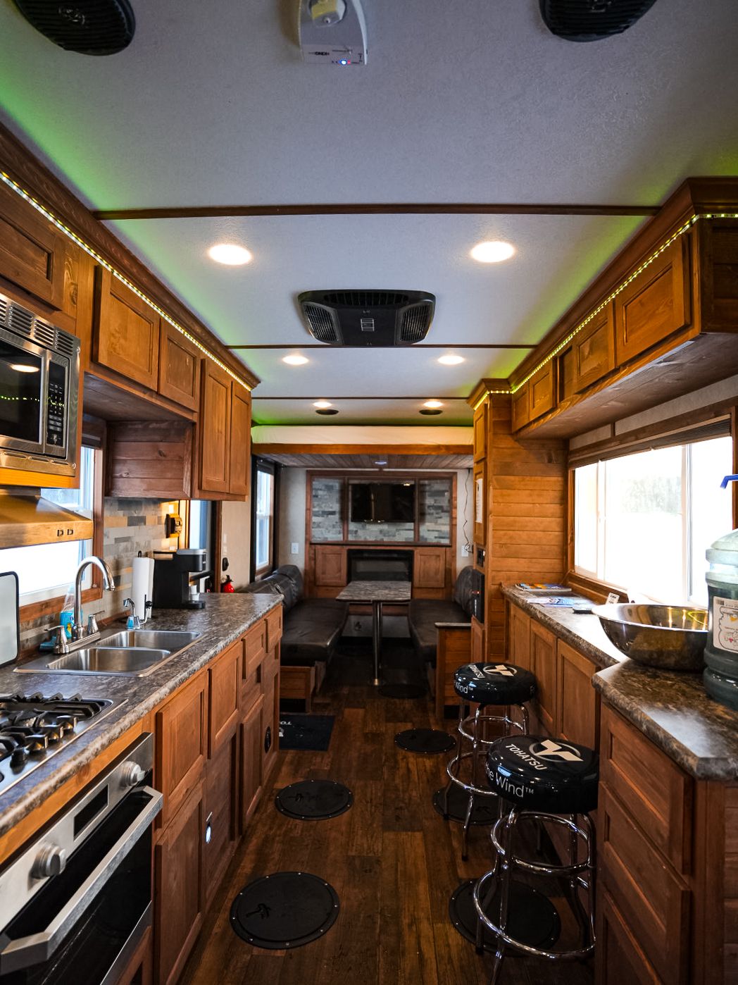 Modern RV interior featuring wooden cabinets, granite countertops, and stainless steel appliances in a galley layout.