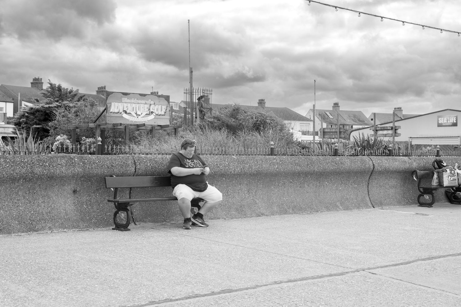 A person sits alone reading on a concrete bench in a black and white vintage outdoor scene.