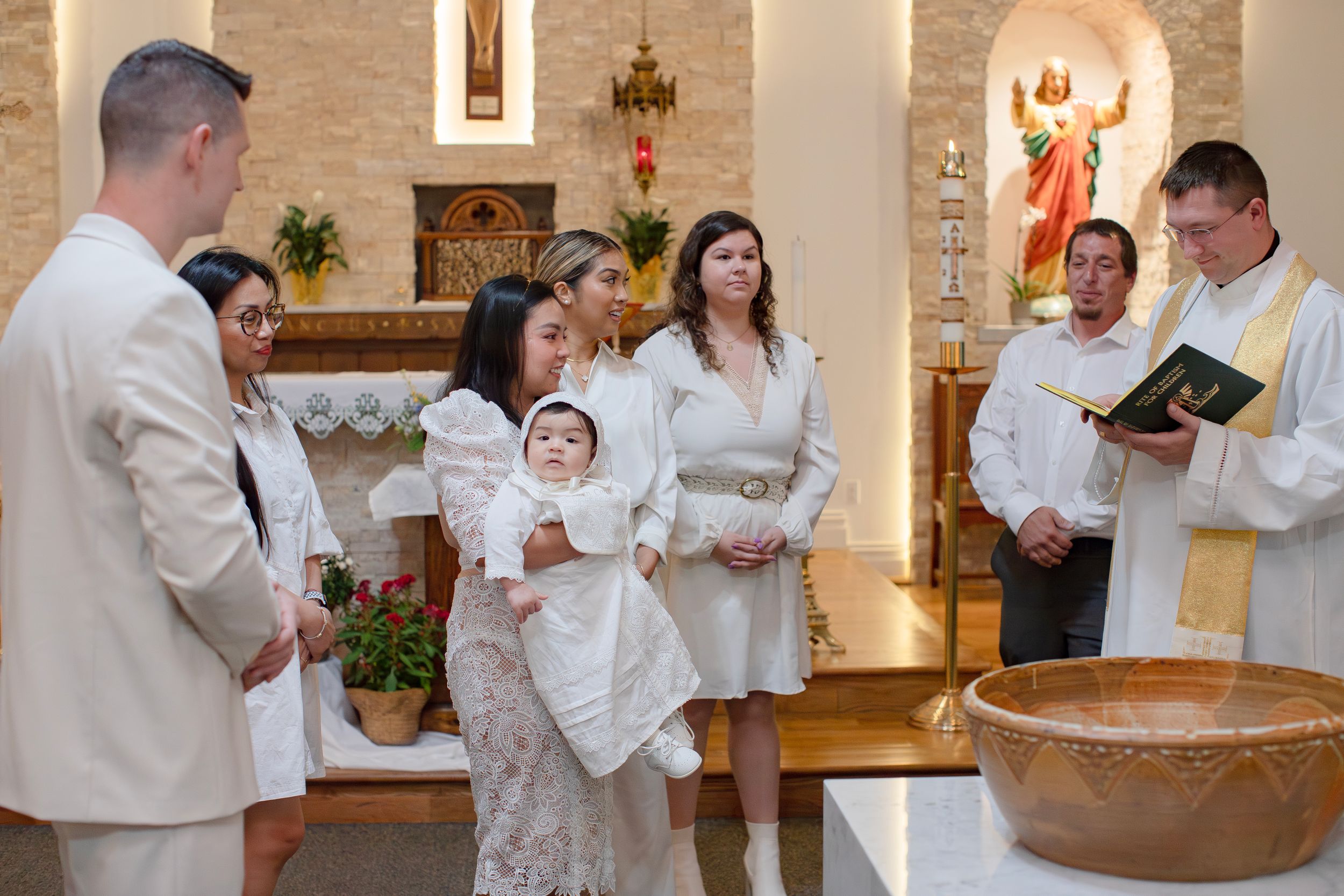 A baptism ceremony taking place in a church with family gathered around the baptismal font.