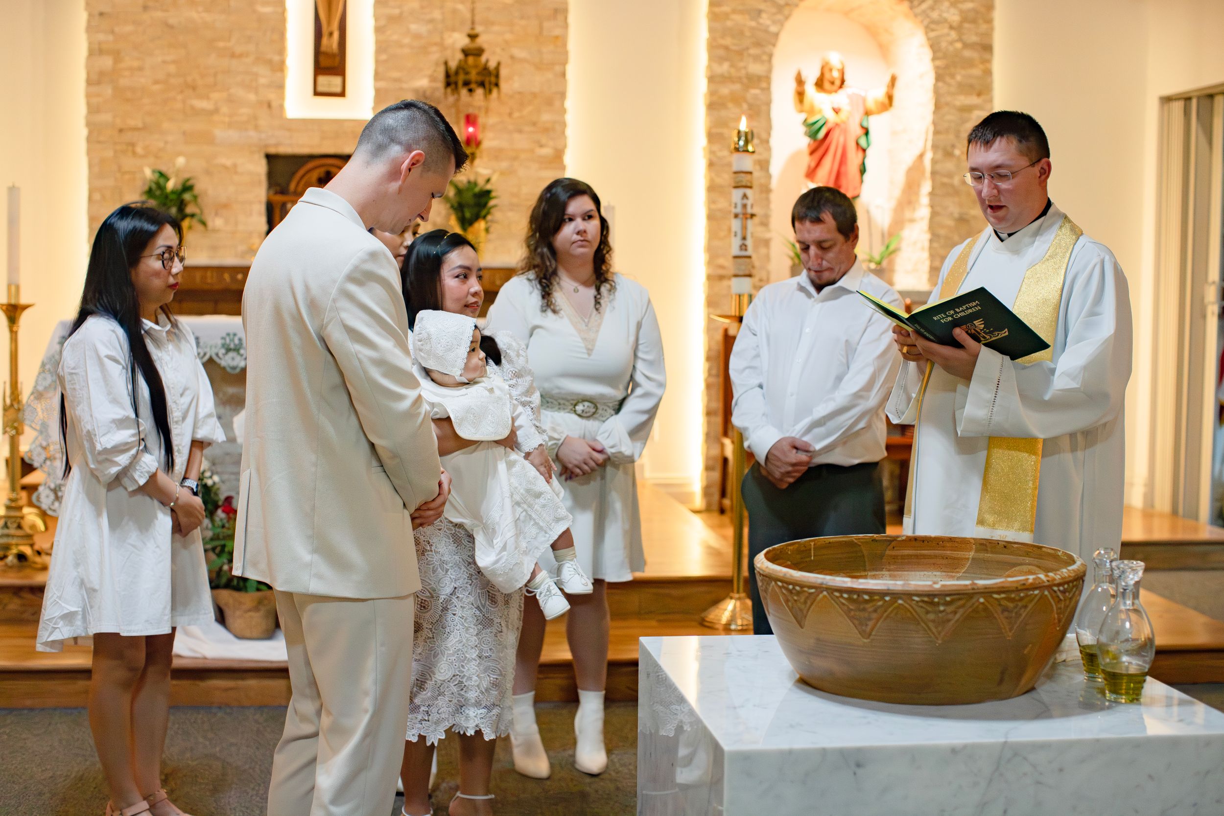 A baptism ceremony in progress as family members gather around in white attire.