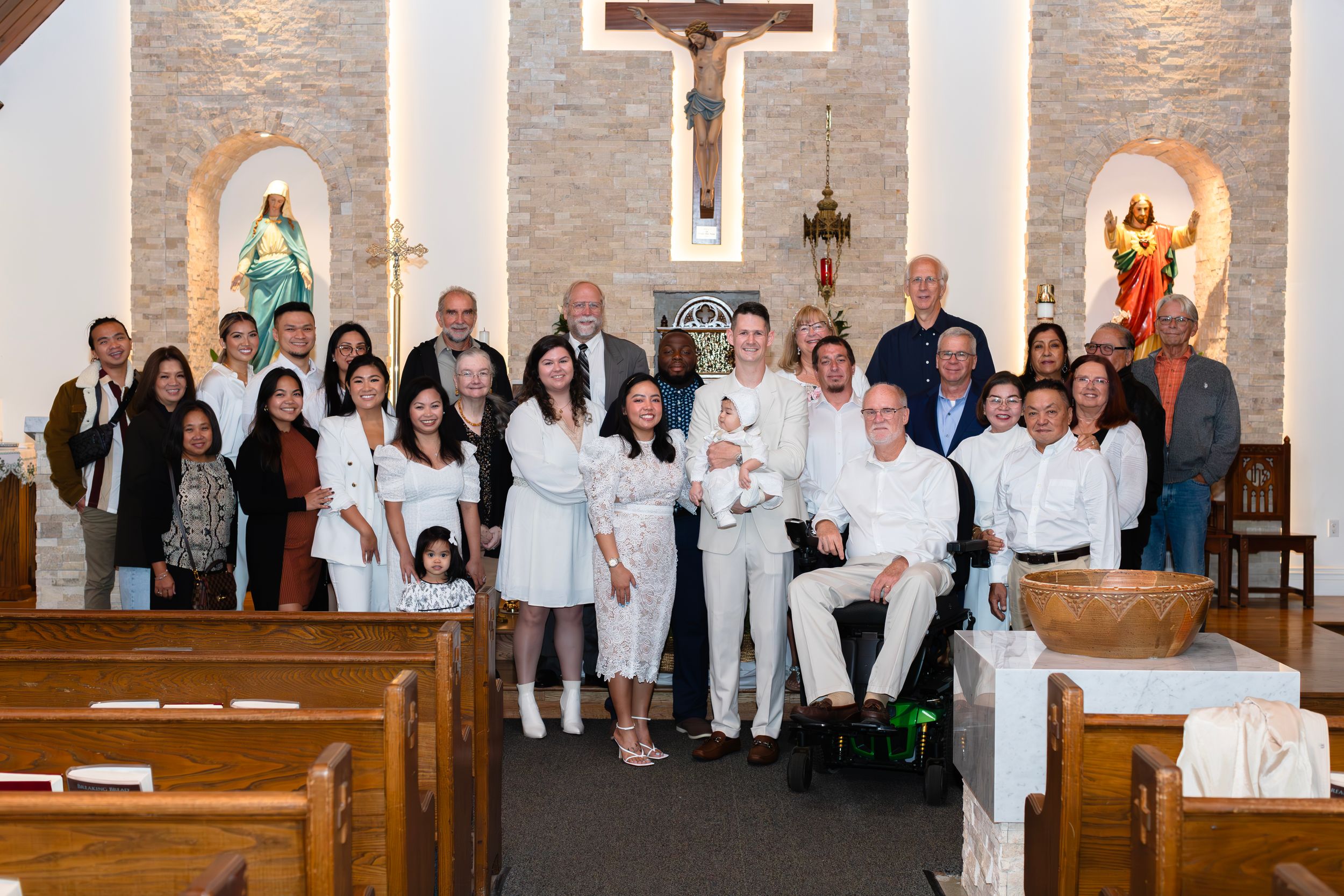 Large group photo of family and friends gathered in church pews after a baptism ceremony.