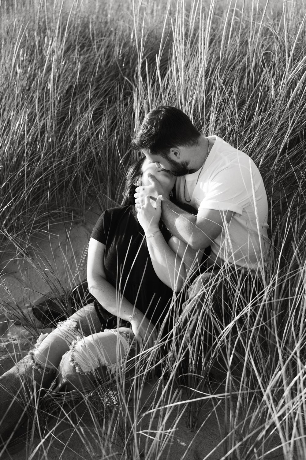 A romantic black and white portrait of a couple sharing an intimate moment among tall grass.