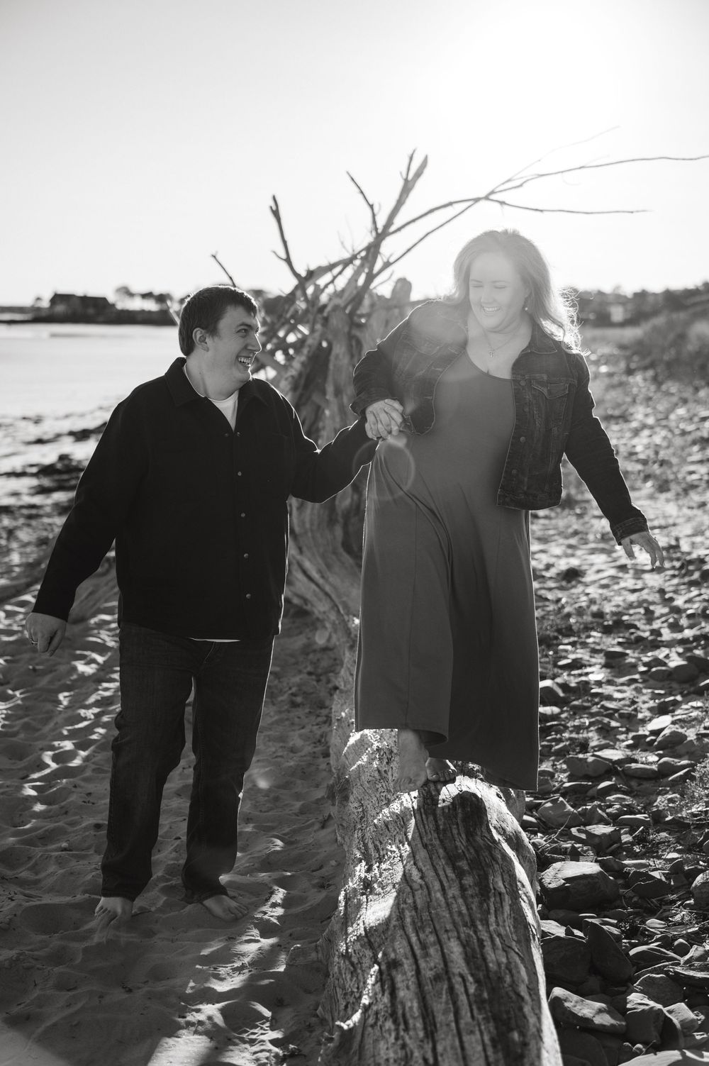 Two people playfully dance together on a rocky beach at sunset.