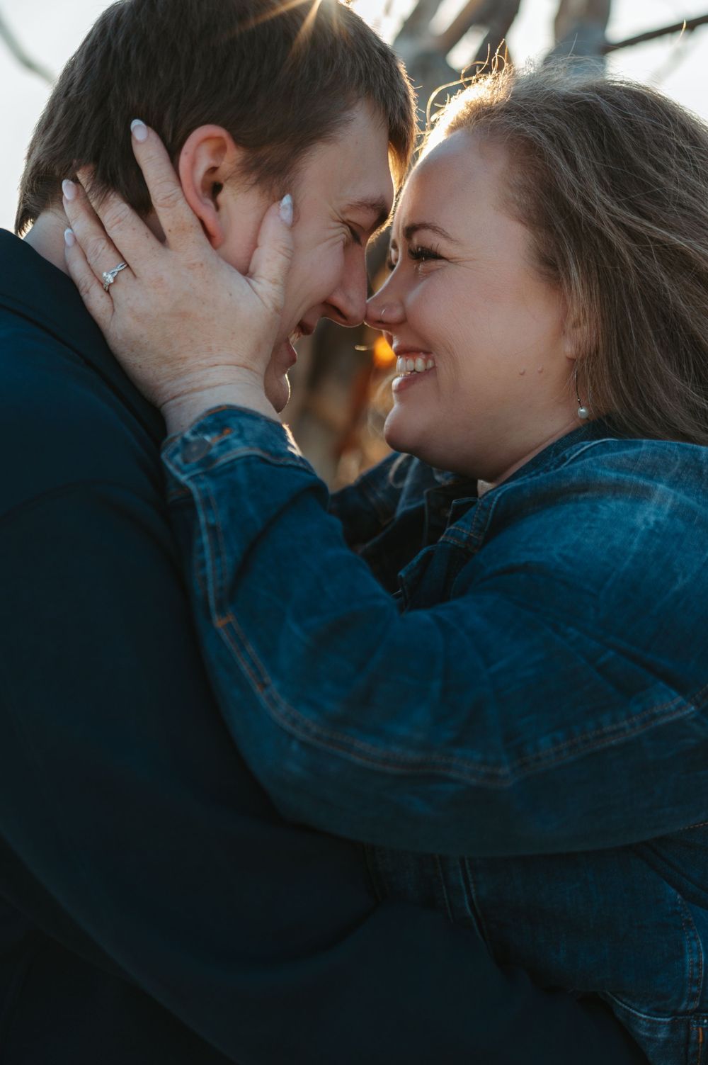 A romantic couple embraces in silhouette against sunlight while wearing denim jackets outdoors.