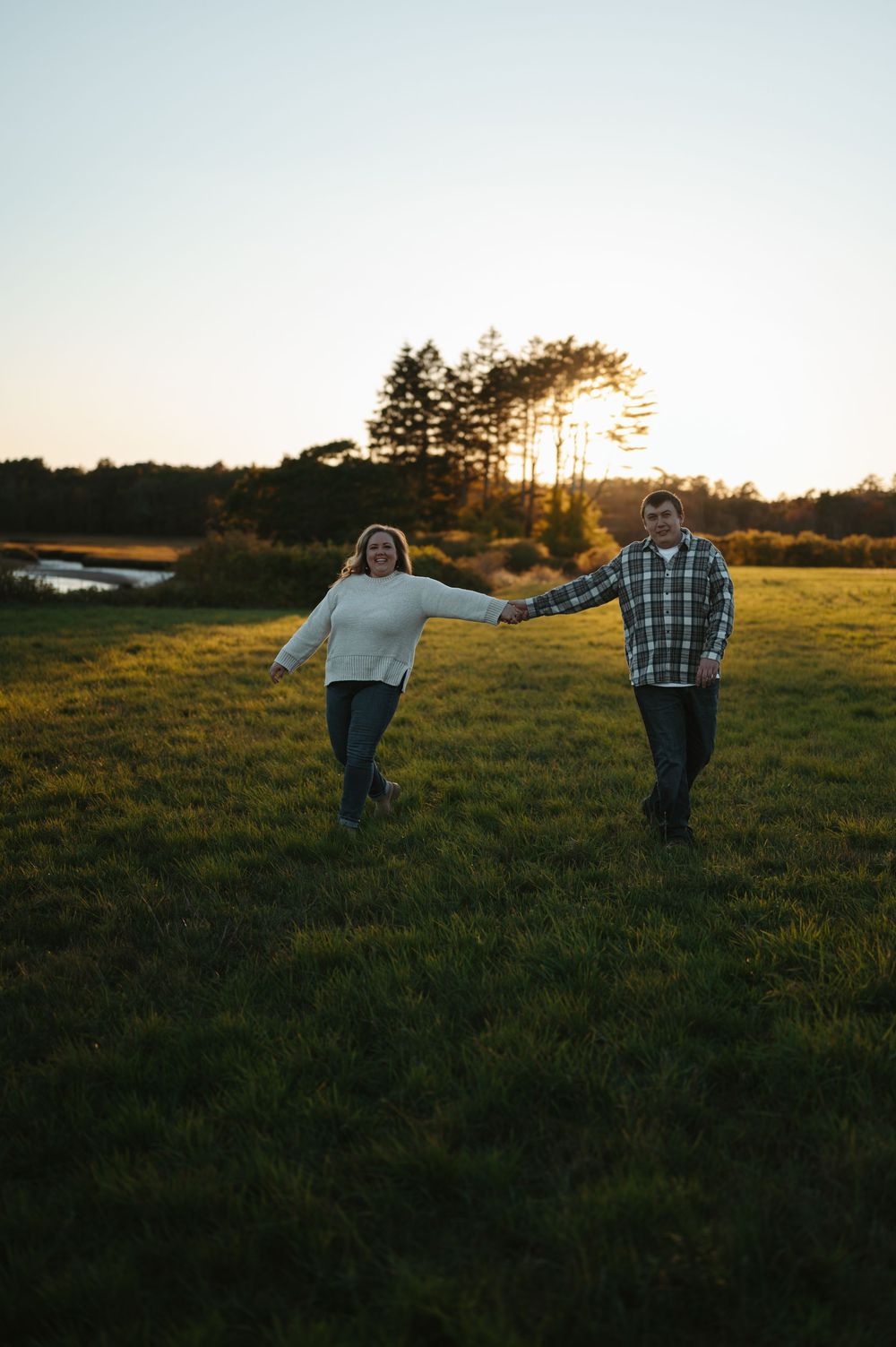 Silhouettes of a couple holding hands in a grassy field at sunset with trees in the background.