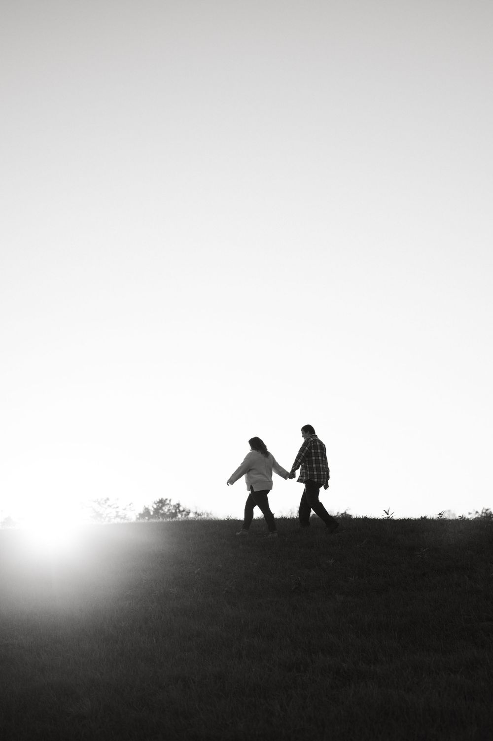Silhouettes of two figures walking along a hilltop against a bright sky in a dramatic black and white landscape.