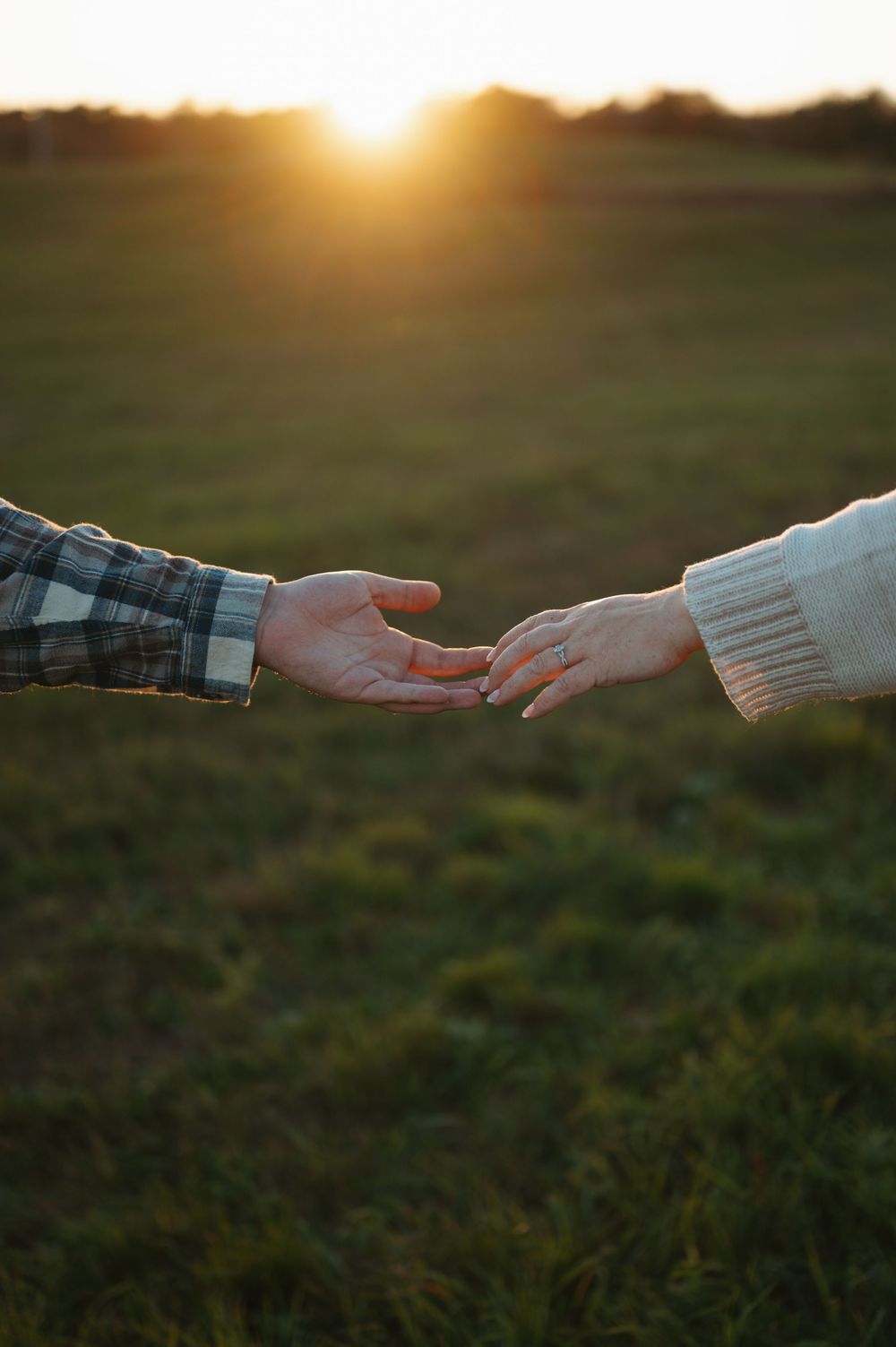 Two hands reaching towards each other against a sunset backdrop in a romantic gesture.