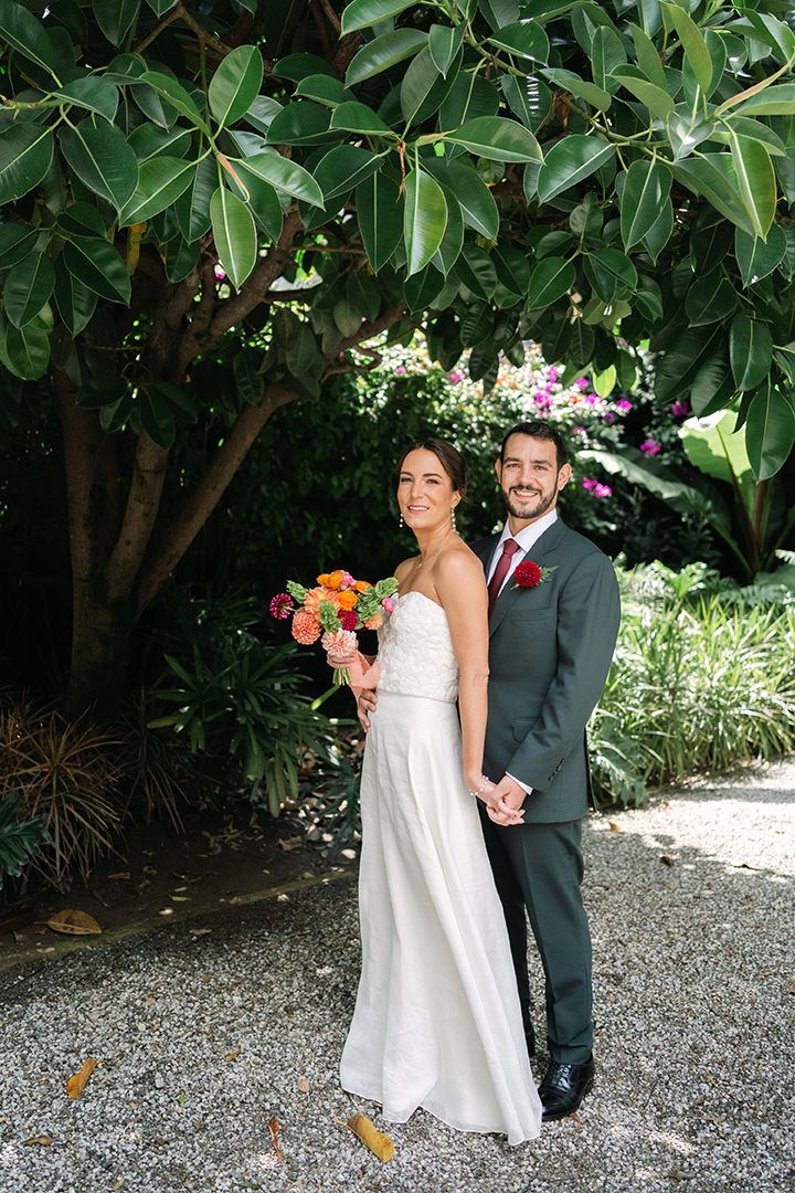 A wedding couple poses on a wooden walkway surrounded by lush tropical palm trees.
