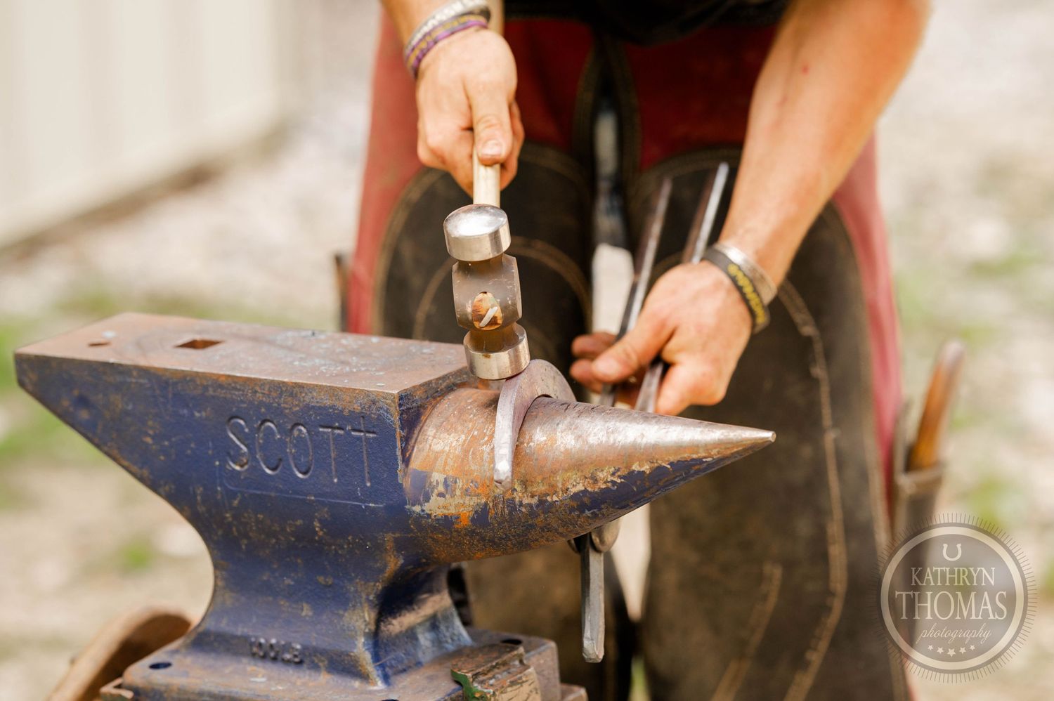 Close-up shot showing metalworking on a blue Scott anvil with hammering tools.