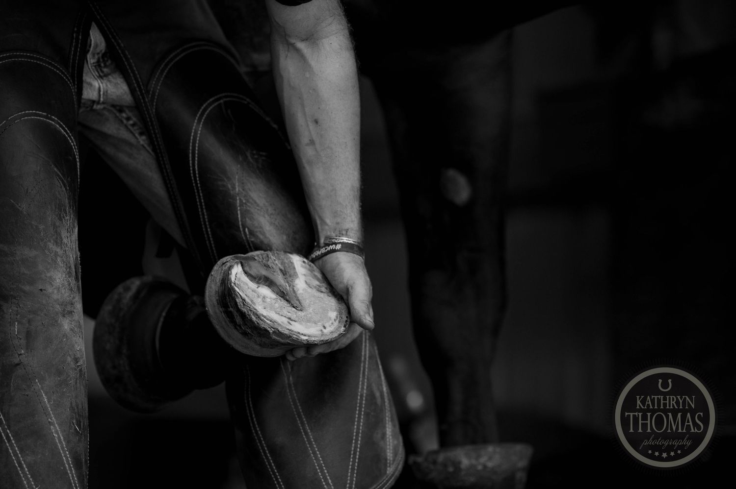 Black and white detail shot of hands working with horse hoof