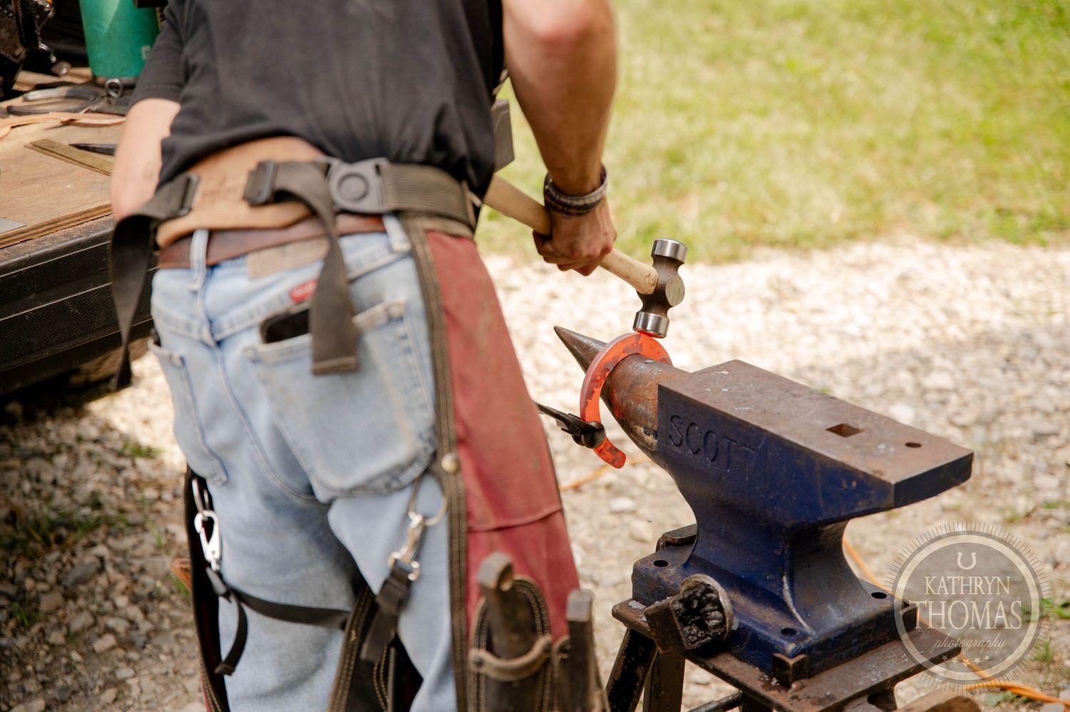 Close-up of hands working with tools at a metal anvil during farrier work.