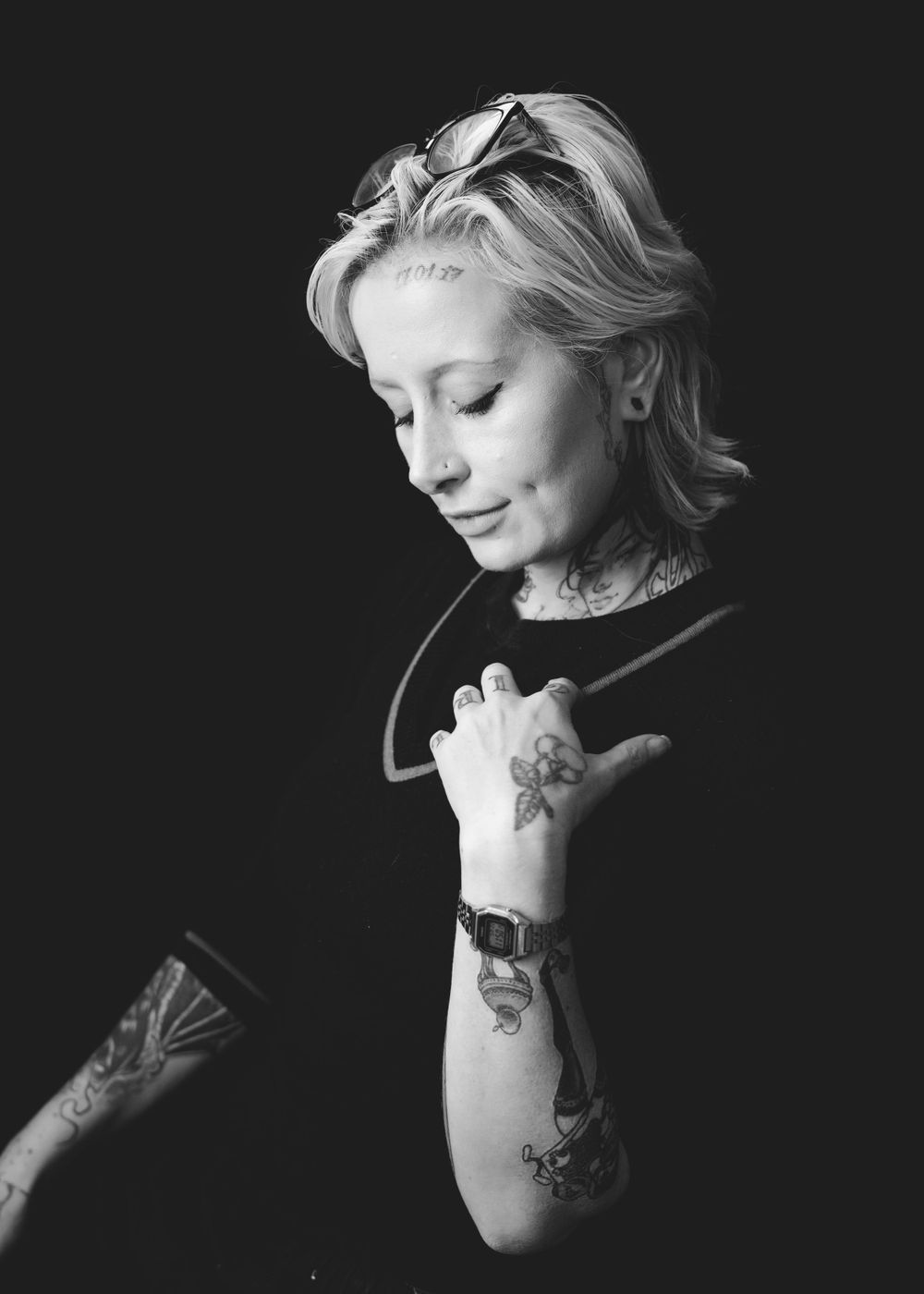 Black and white portrait showing person in contemplative side profile pose with visible arm tattoos.