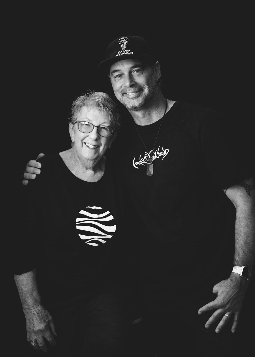 A black and white portrait shows two people embracing and smiling together, one wearing glasses and a zebra print top.