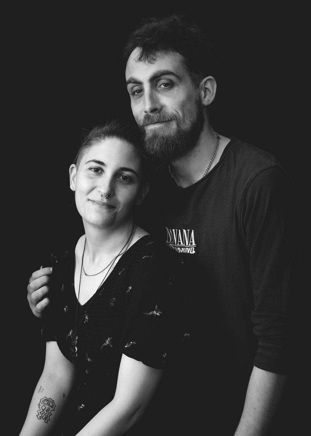 Black and white portrait of a couple smiling together, with the person on the right wearing a Nirvana t-shirt.