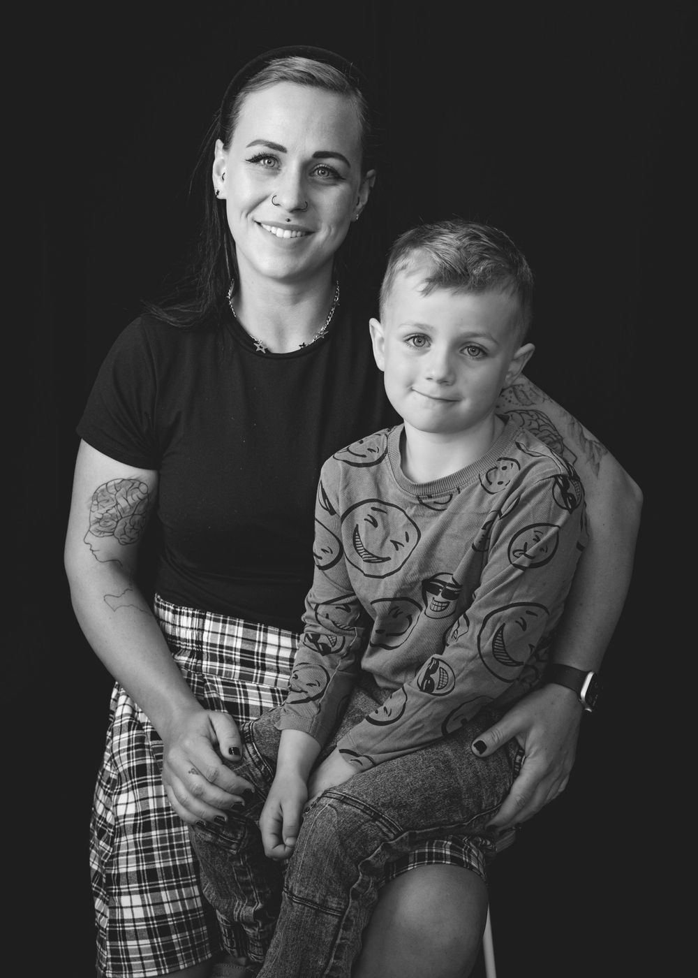 A black and white portrait of an adult in a black top and plaid skirt with a young child wearing a patterned shirt.