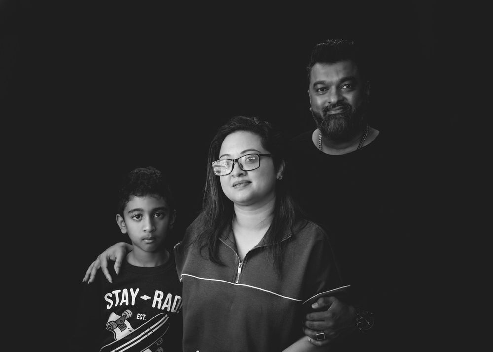 A black and white portrait of three people smiling together, with one wearing glasses and another wearing a Stay Rad shirt.