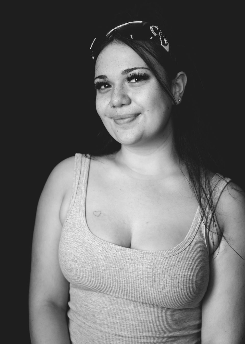 A black and white portrait of someone wearing a bandana and tank top, smiling warmly at the camera.