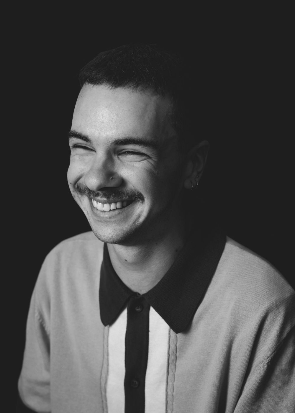 A black and white portrait shows a joyful candid moment with someone wearing a collared shirt and genuine smile.