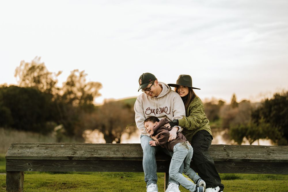 Two friends laugh together while sitting on a wooden fence at sunset in a grassy field.