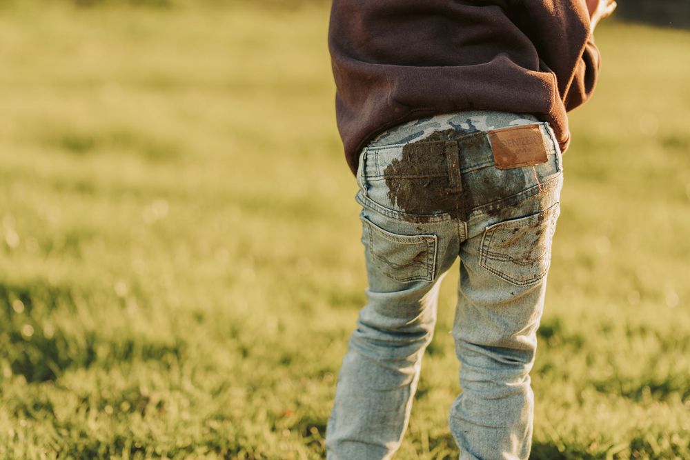 Close-up view of muddy jeans from behind as someone stands in a grassy field at sunset.