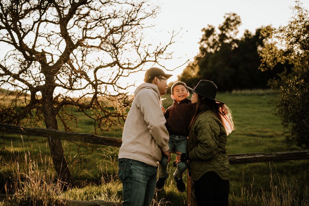 A group stands together in a scenic rural setting during golden hour with bare trees and green pastures in the background.