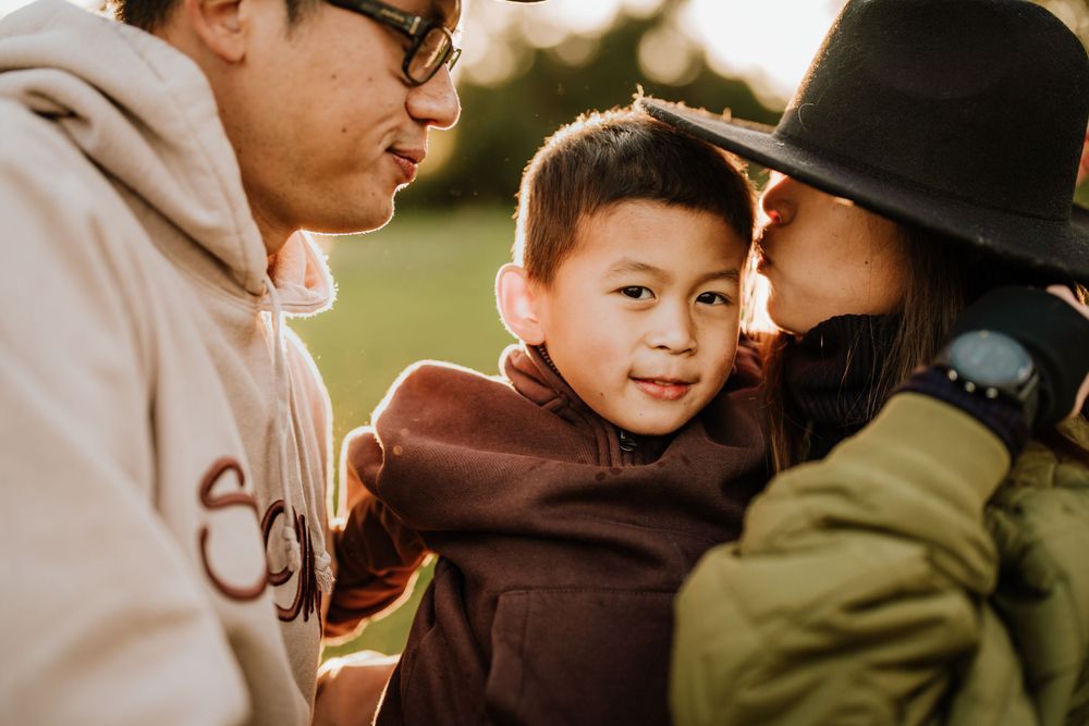Three people share an intimate moment together outdoors during golden hour in a close familial scene.