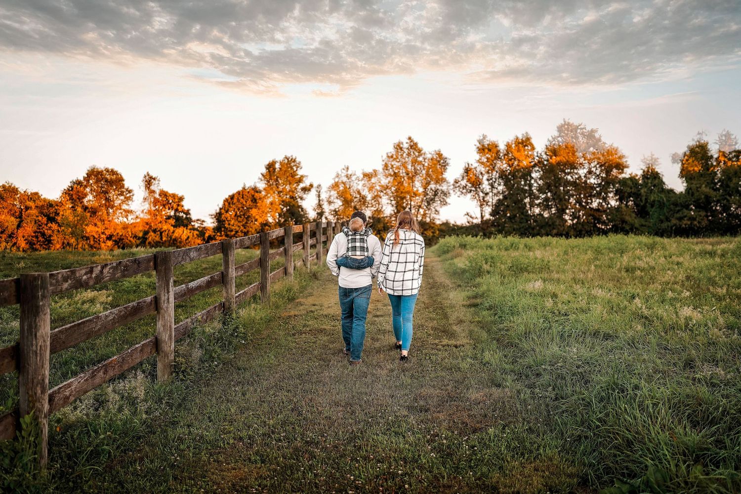 A couple sits on a blanket with their dog in a grassy field at sunset during autumn.
