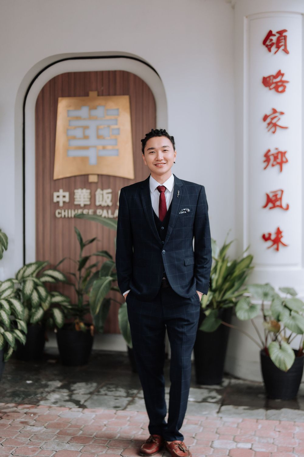 Person in navy suit standing in front of Chinese restaurant entrance with traditional decorations.