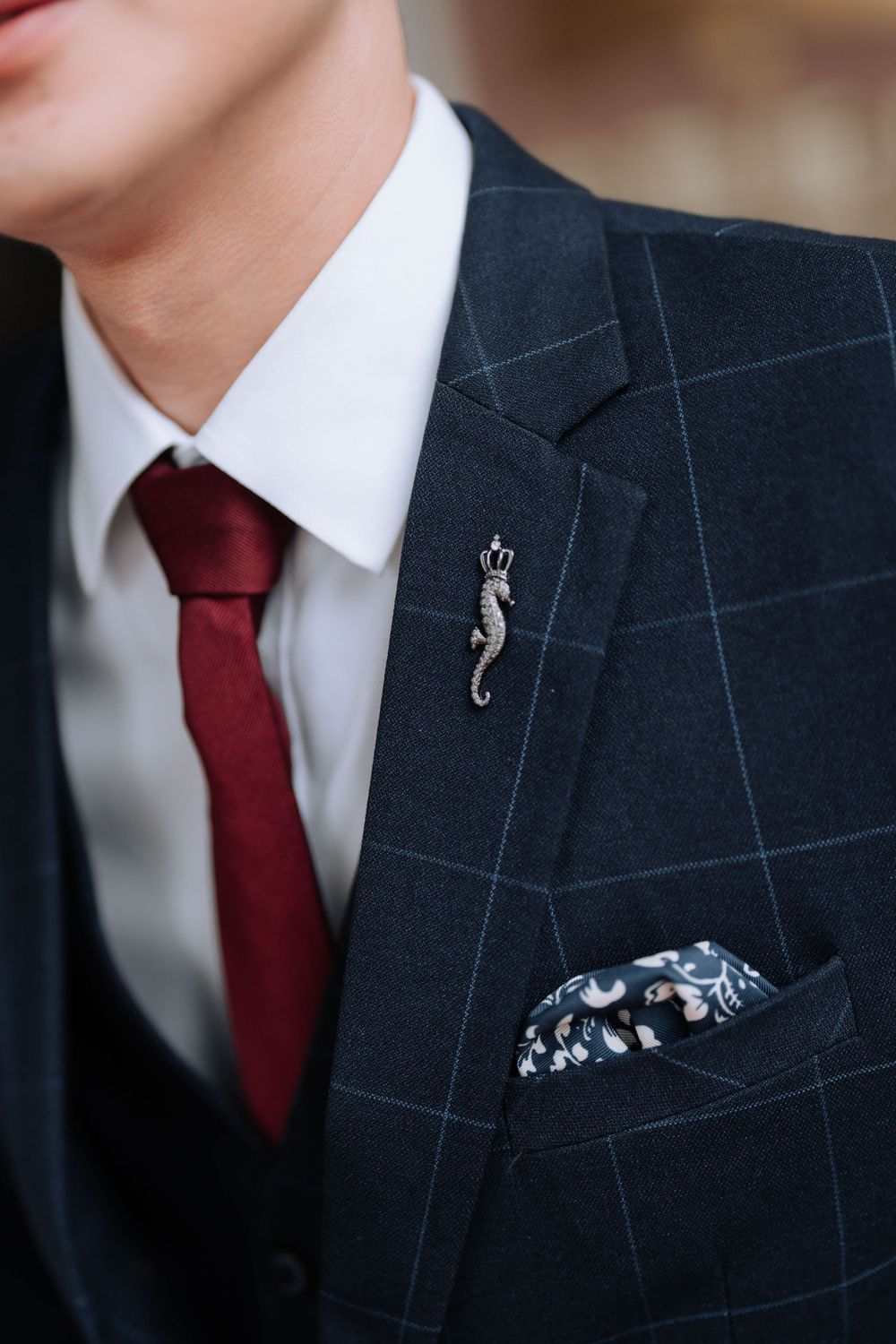 Detail of navy windowpane suit with red tie and decorative cat lapel pin.
