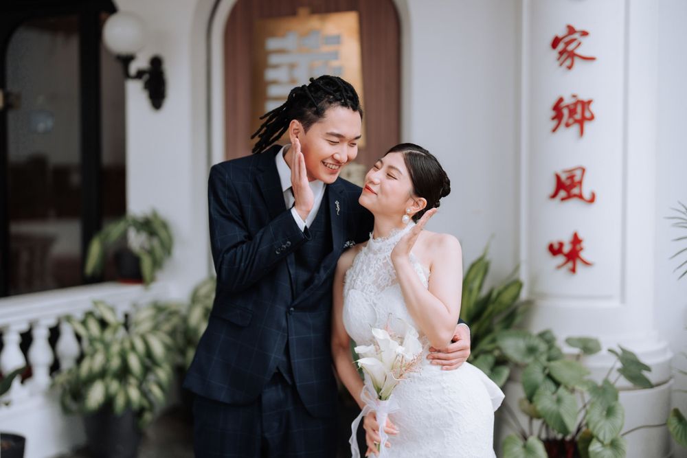 A playful wedding photo showing a couple laughing together in front of an Asian-style building.