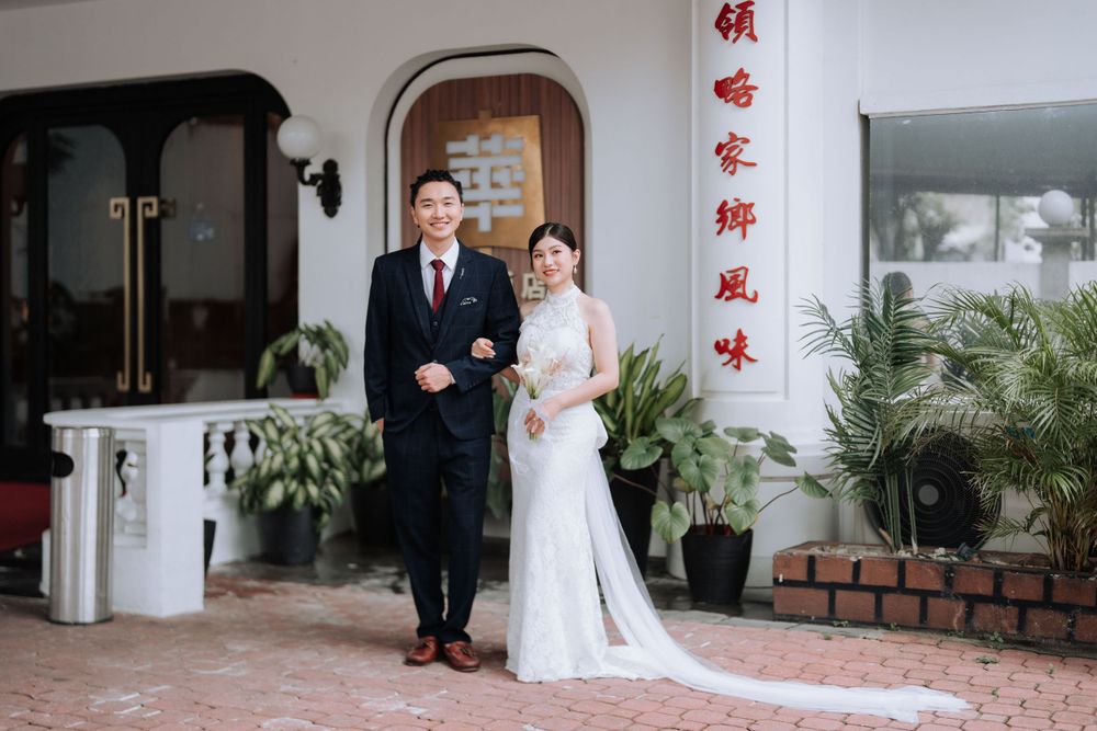 A formal wedding portrait of a couple in front of a Chinese-style building with red characters.