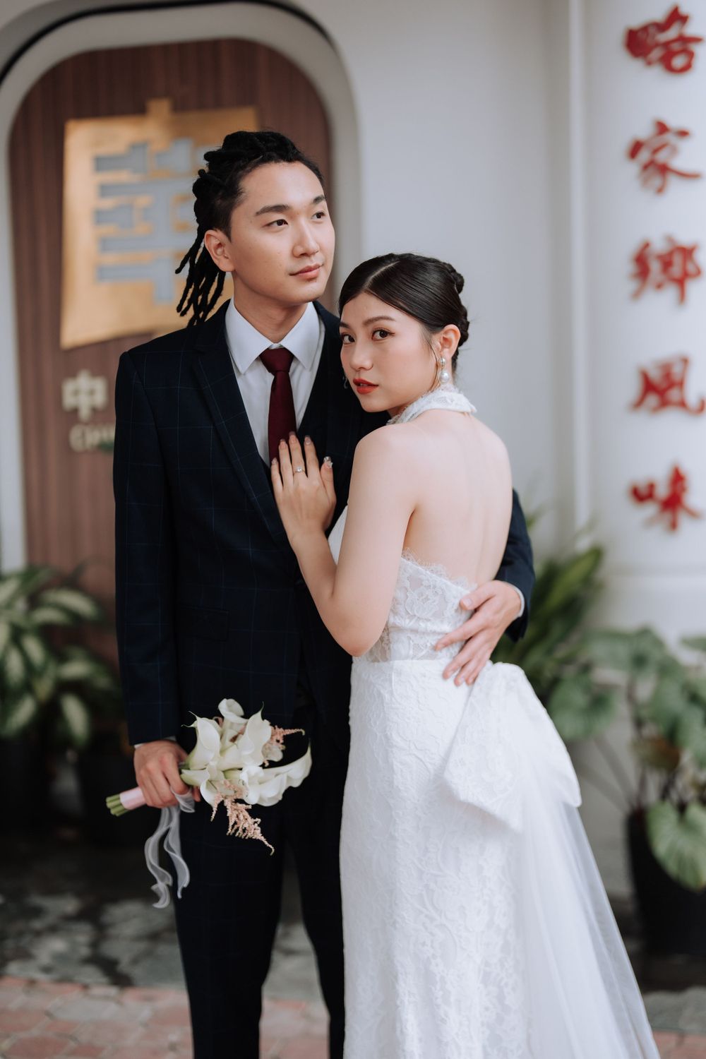 A romantic wedding portrait featuring a couple in elegant attire against a white wall.