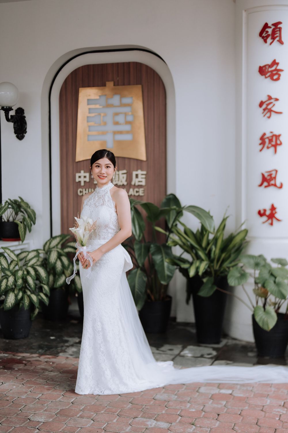 A bride in a white lace halter dress poses elegantly against a Chinese building facade.