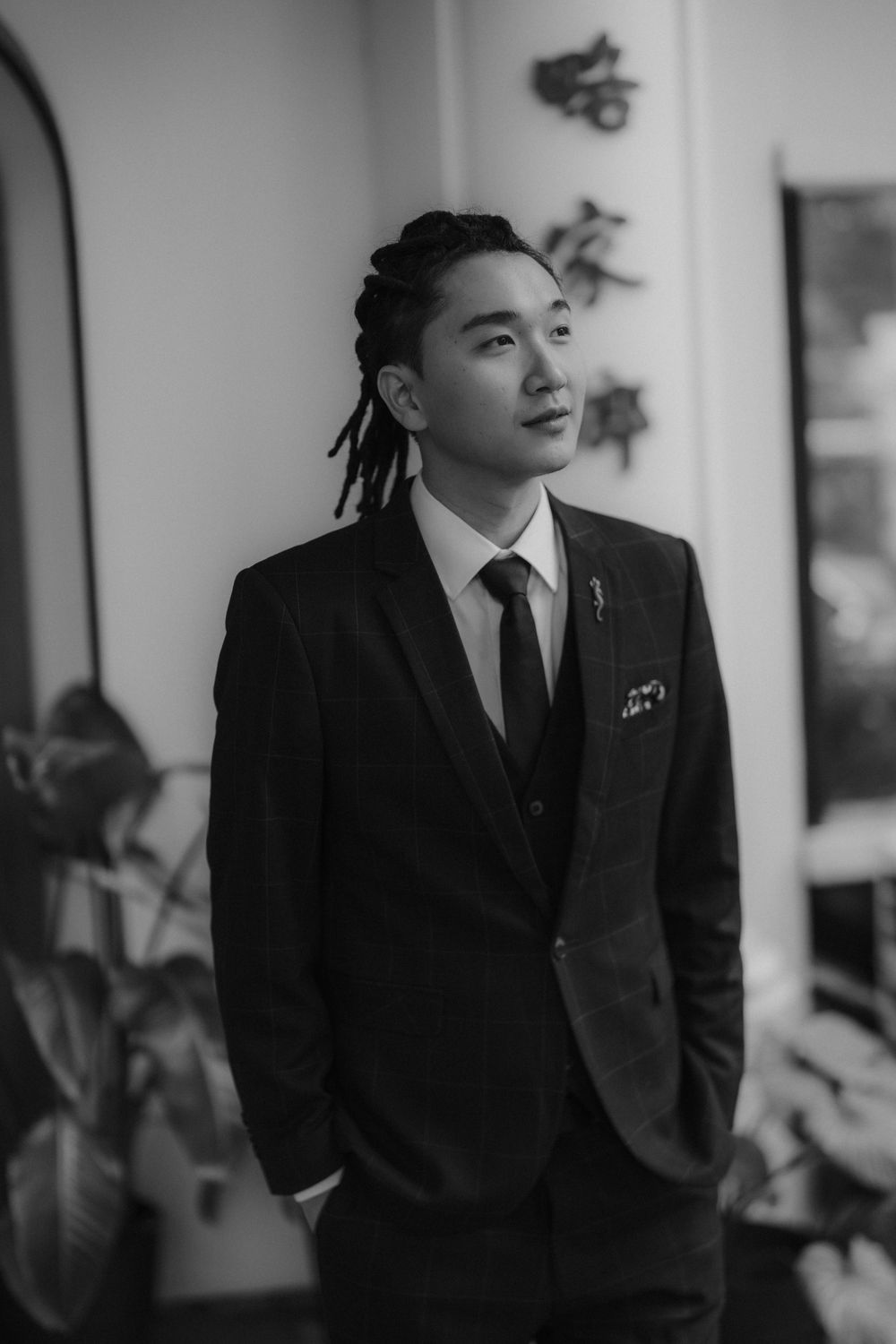 Black and white portrait of someone in a suit with styled dreadlocks against an archway.