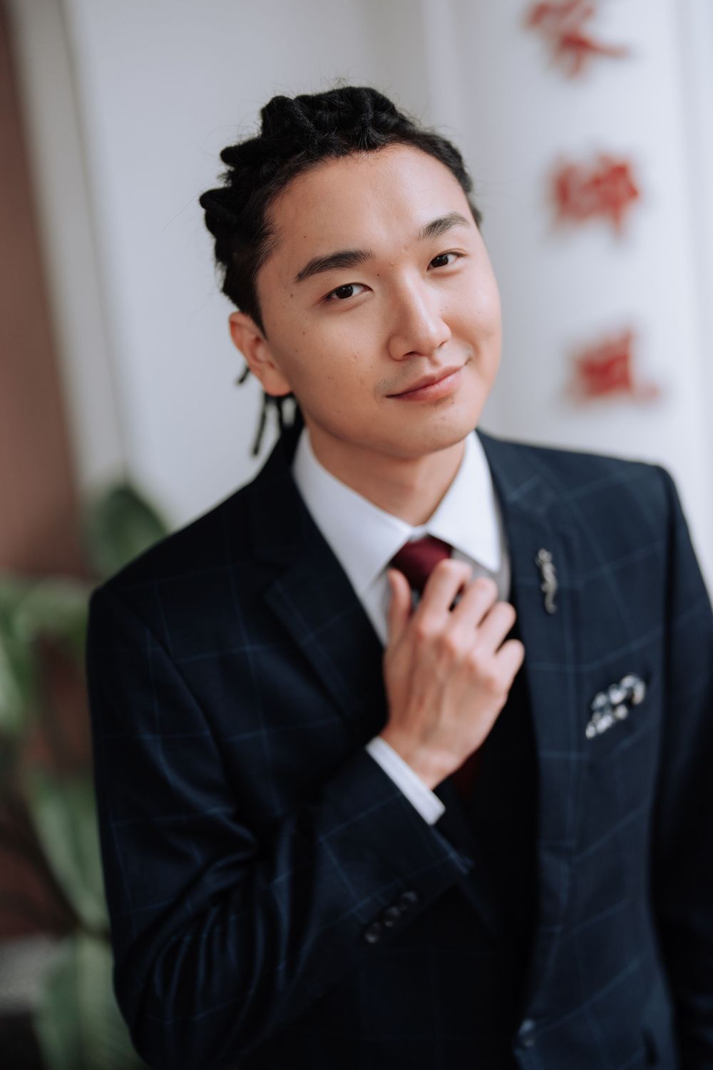Close-up portrait of someone wearing a dark suit and red tie against a light background.