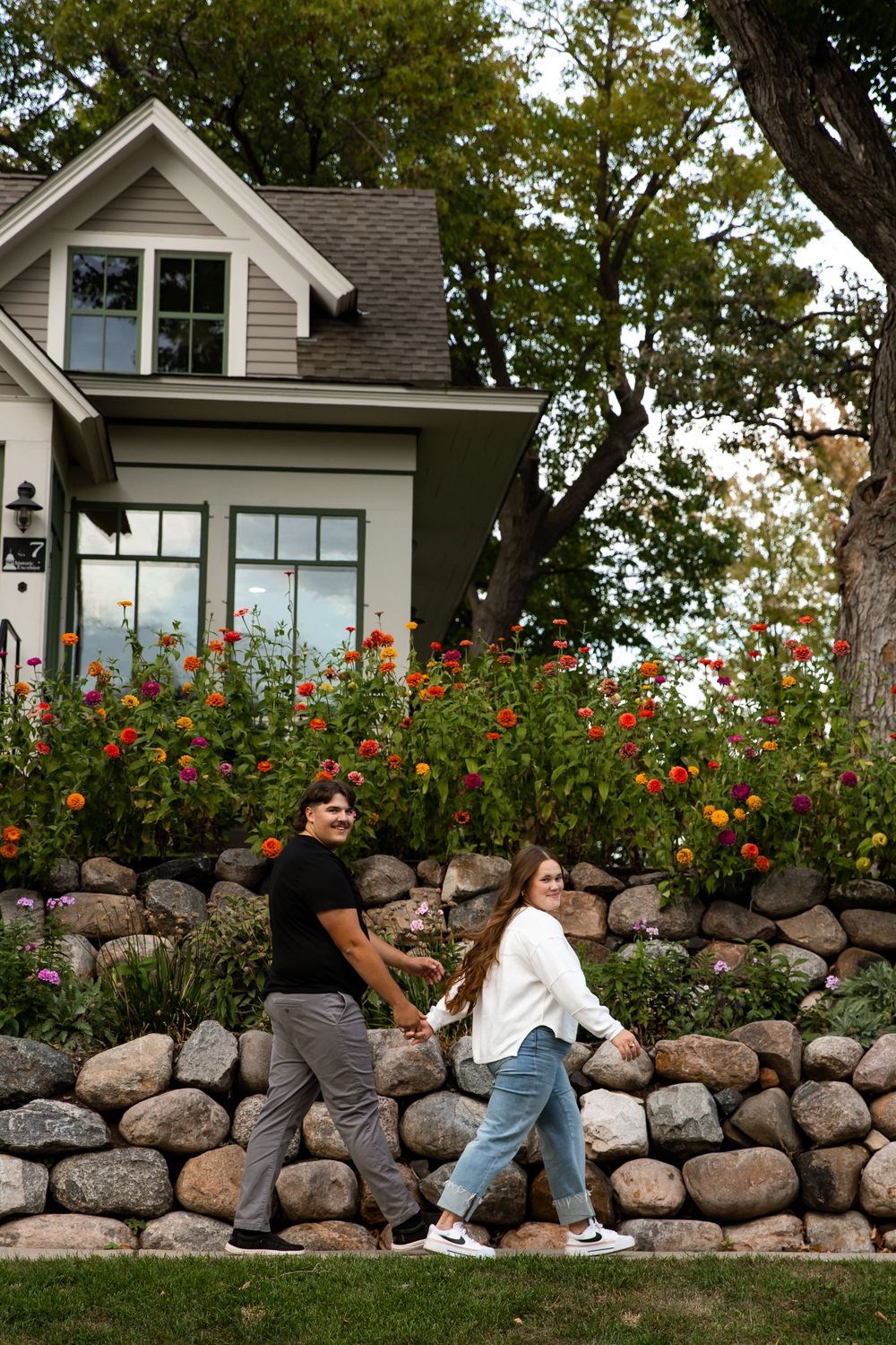 A series of four photos showing people sitting on a rustic stone wall with red flowers and a white house in the background.