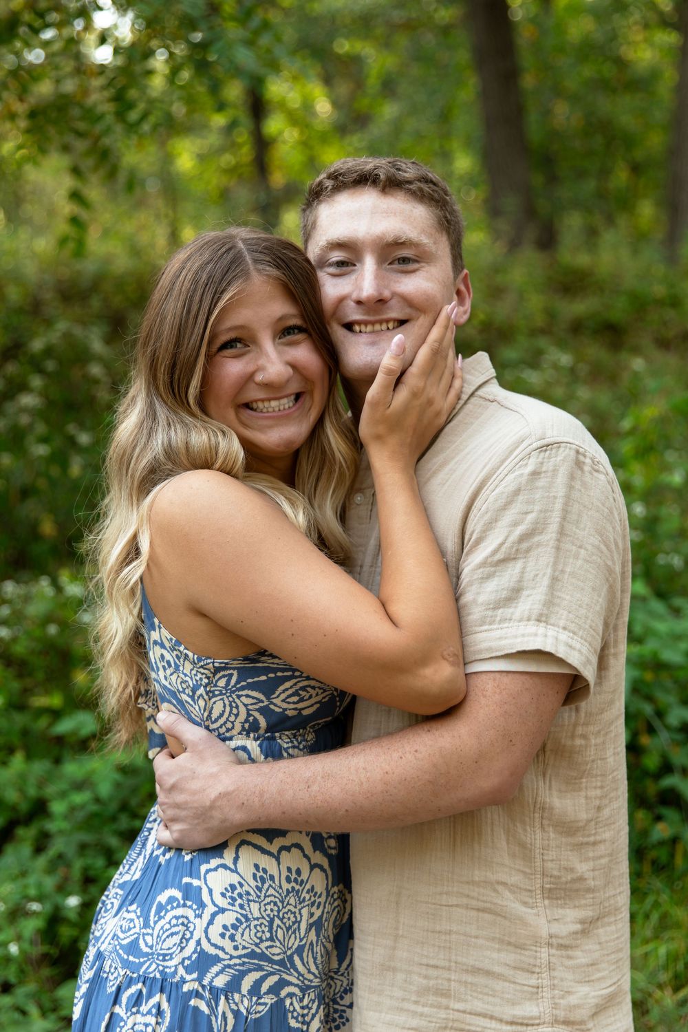 A couple embraces and laughs together during an outdoor photo session in a lush green forest setting.